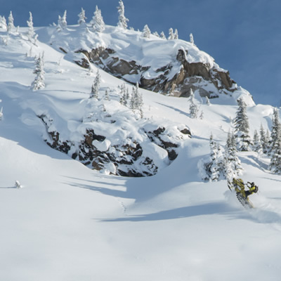 A guy in the distance on a snowmobile sledding on a large snow-covered pristine mountain.  