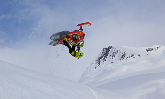 Ashley Chaffin is upside down in the air, doing a backflip on her snowmobile.