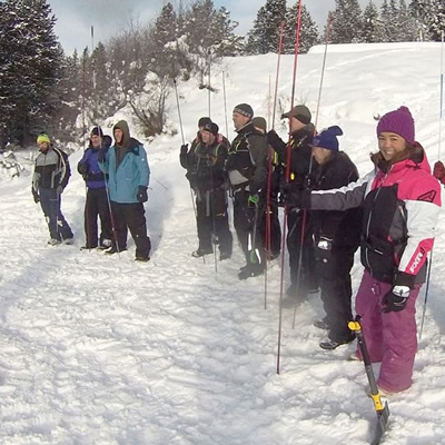 Group of people participating in Avalanche Awareness seminar, outside in snowy field. 