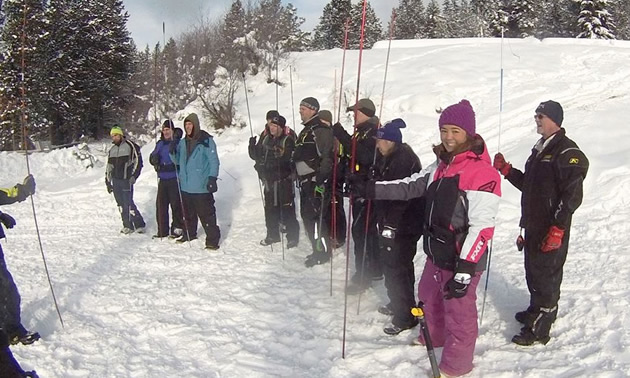 Group of people participating in Avalanche Awareness seminar, outside in snowy field. 