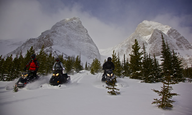 Three snowmobilers in a dramatic mountain landscape