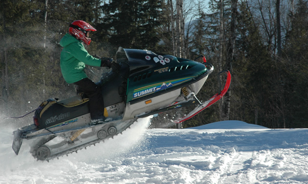 Close-up of a small person taking a snowmobile into a jump.