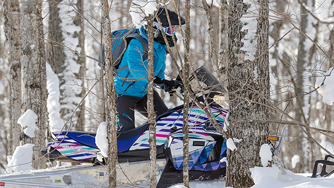 Picture of woman riding a snowmobile through the woods. 