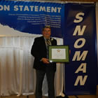 Man in dress suit standing on a stage holding a framed certificate.