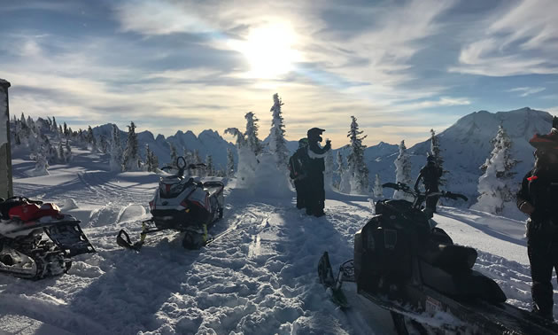 Group of snowmobilers on mountain top. 