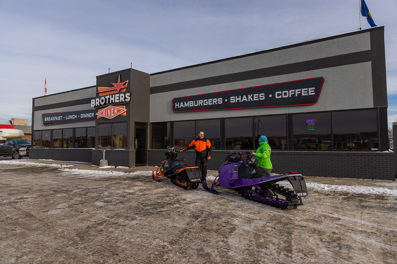 Two snowmobilers park and pose in front of Brothers’ Diner in Whitecourt, Alberta.