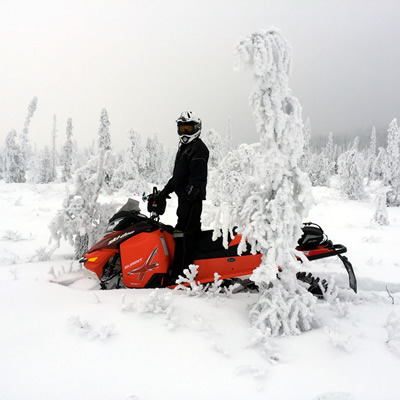 A snowmobiler standing on his ride next to a snowy tree in Wildcat Hill Provincial Park near Hudson Bay, Saskatchewan. 