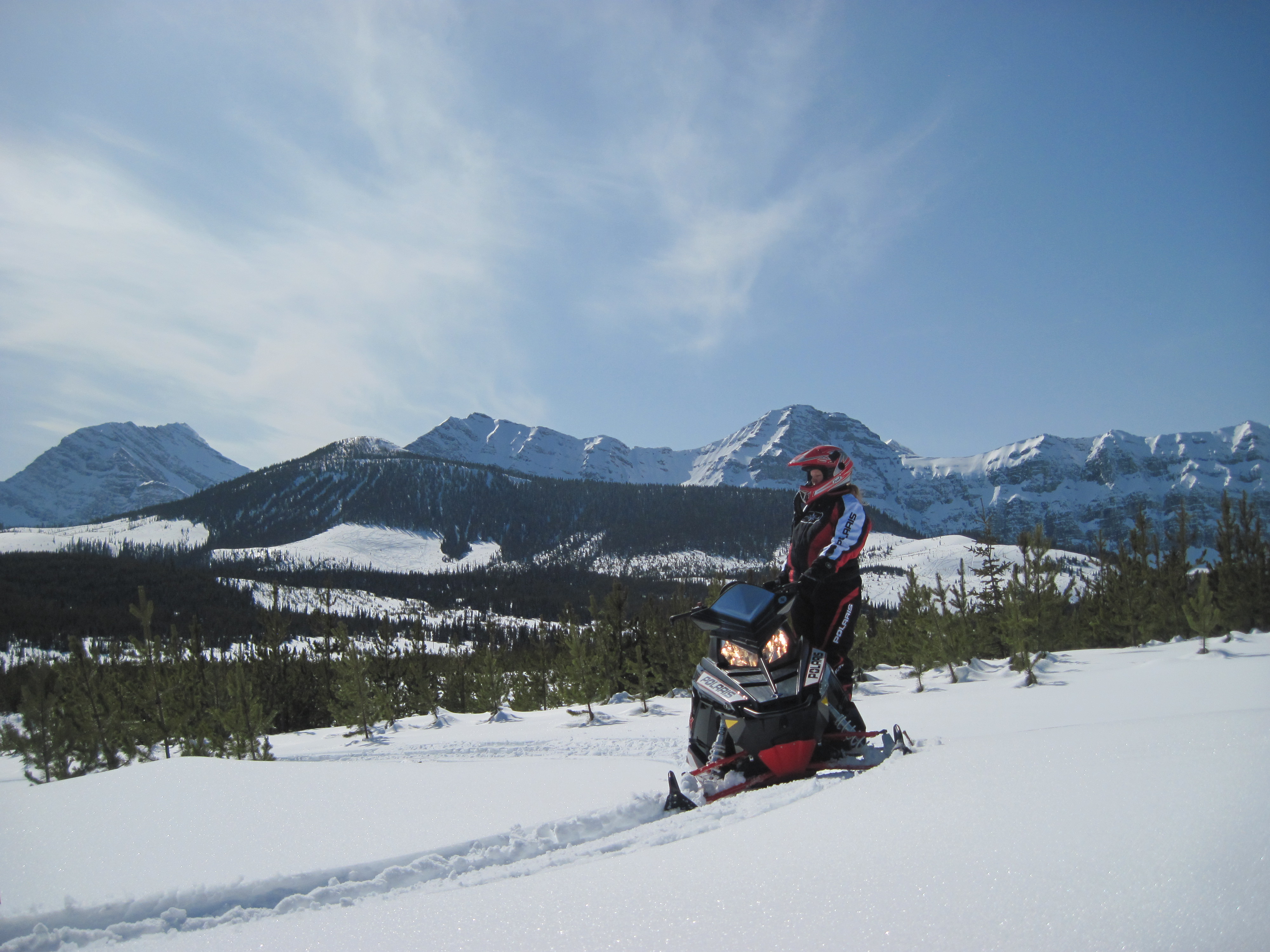 Lone snowmobile and rider overlook a mountain panorama on a bright winter day