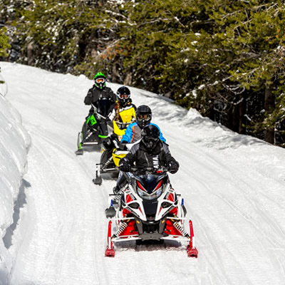 Row of snowmobilers out on a snowy trail. 