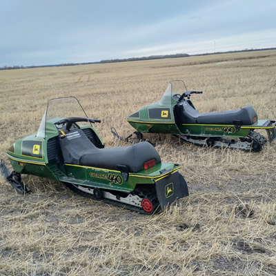 Two John Deere Cyclone sleds sitting out in a field. 