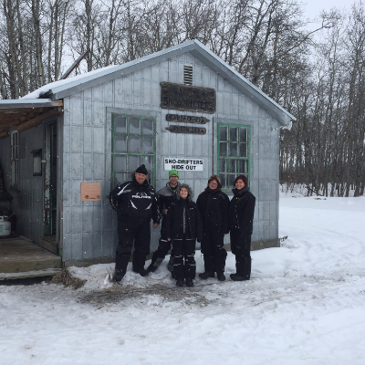 Members pose in front of the Sno-Drifters' Hide Out warm-up shelter. This shelter is located just south of Kamsack before Rhein.