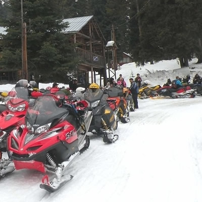 Line up of snowmobiles and people getting geared up. 