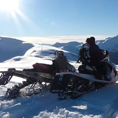 Panorama picture of sled in foreground with blue skies and mountains in background. 