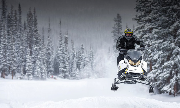 Picture of snowmobiler riding along snowy trail. 