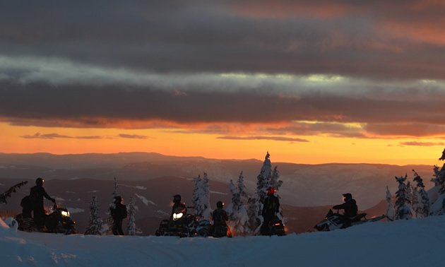 Six sledders on a ridge, against a sunset sky