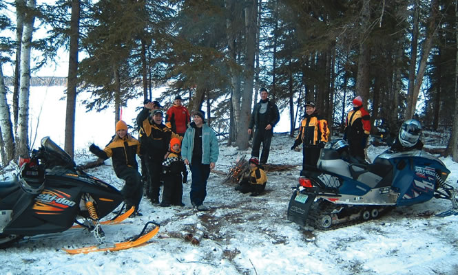 a group of people in snowsuits in the forest in winter around a campfire