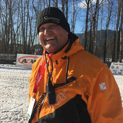 Man dressed in orange winter coat smiling. 