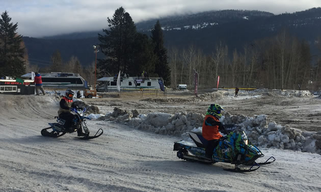 Two kids on snowmobiles racing on track. 