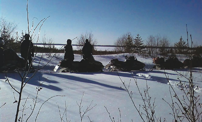 snowmobilers on a lakeside trail