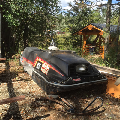 Picture of rusting snowmobile in backyard. 