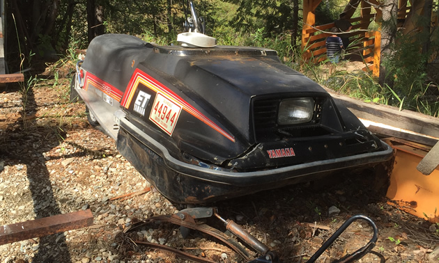 Picture of rusting snowmobile in backyard. 