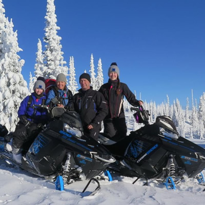 Group of snowmobilers at top of mountain with blue sky in background. 