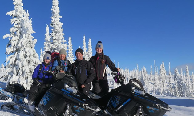 Group of snowmobilers at top of mountain with blue sky in background. 