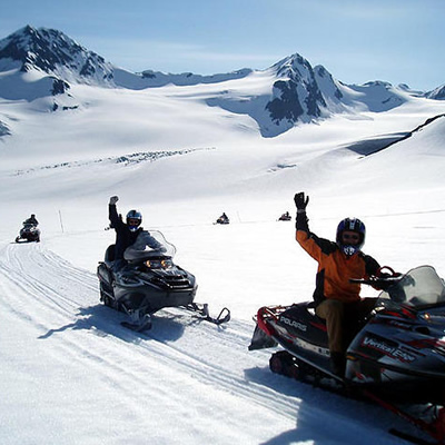 A group of Alaskan snowmobilers riding down a snowy mountain trail. 