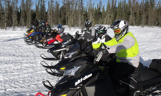 Snowmobilers lined up in a row, ready to ride. 