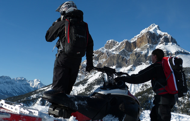 two snowmobilers looking at the mountains. 