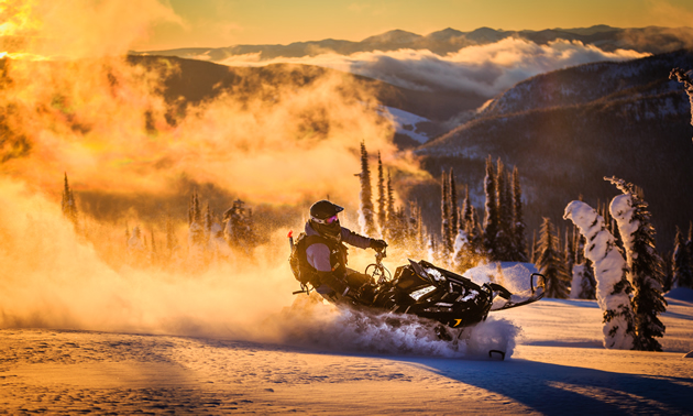 Billy Stevens snowmobiling with the sunset behind him. 