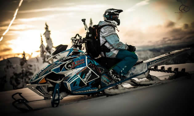 A man sitting backwards on a blue snowmobile. 
