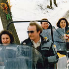 Photo of two people driving a two seater snowmobile and towing a couple behind in a cutter on their way to a wedding. 