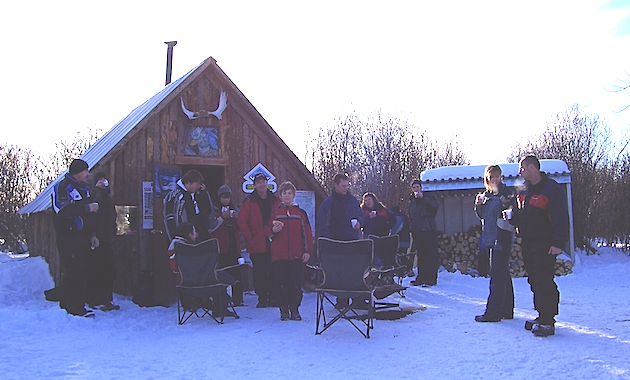Snowmobiling warm-up shelter with a group of sledders gathered outside it.