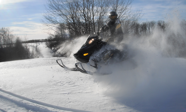 A man on a black sled playing in the powder. 