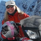 A blonde haired lady in red sitting on her snowmobile. 