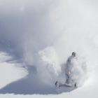 Photo of two snowmobilers riding down a steep mountain with lots of fresh snow.