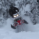 A rider in all black on a red and white snowmobile. 