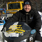 A man in black sitting on a yellow snowmobile. 