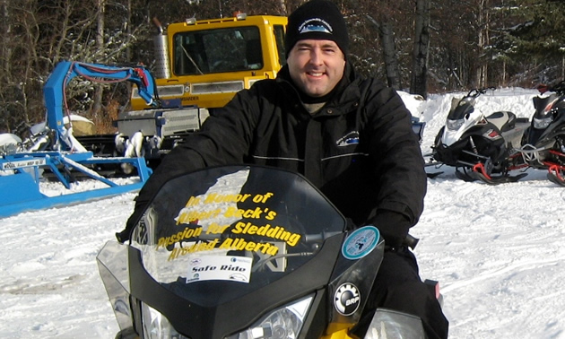 A man in black sitting on a yellow snowmobile. 