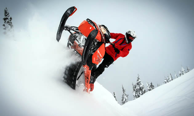 A rider on an orange Ski-Doo sidehilling. 