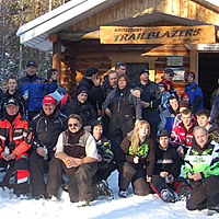 A group of snowmobilers standing in front of a cabin. 
