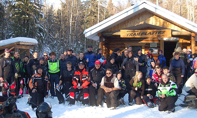 A group of snowmobilers standing in front of a cabin. 