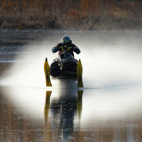 A man riding a snowmobile really fast over open water. 