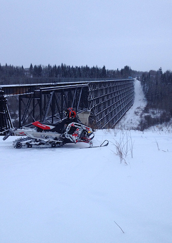 A snowmobile parked in front of the Burnt Beaver river trestle bridge on the Iron Horse Trail, Cold Lake, AB.