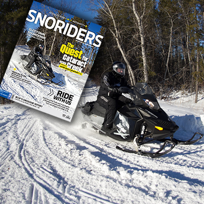 A snowmobiler on a black sled going around a corner on a trail. 