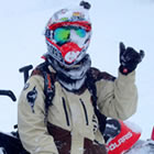 A young man sitting on a black and red sled holding his hand up in the air. 