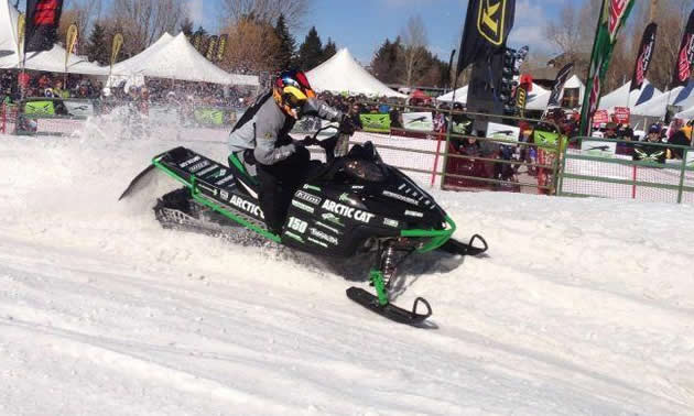 A guy spinning the track on a red and green snowmobile. 