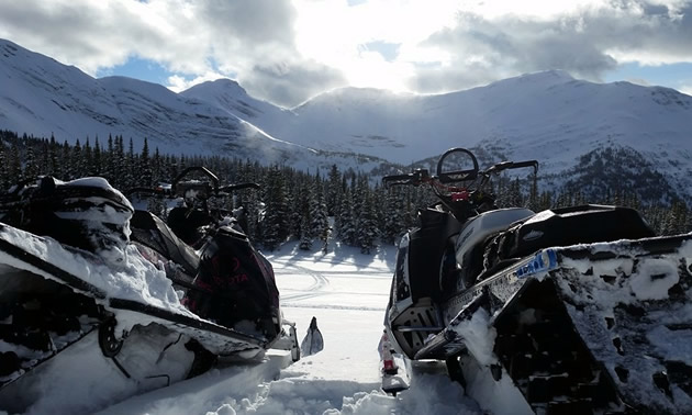 Two snowmobiles parked looking at the Hasler mountain range. 