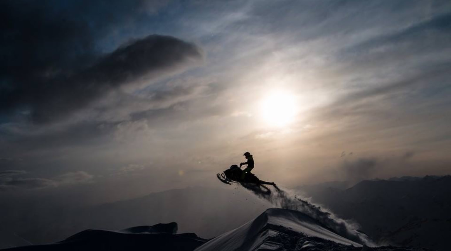 A snowmobiler jumping with the sunset in the background. 